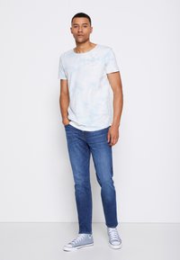 Camiseta de tie-dye azul claro con cuello redondo, combinada con vaqueros azul oscuro y zapatillas azul claro. Diseño sencillo, estilo casual.