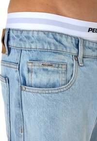 Ανοιχτό μπλε τζιν παντελόνι με καφέ δερμάτινη ετικέτα, αντίθετη πορτοκαλί ραφή και μεταλλική ετικέτα λογότυπου στην πίσω τσέπη.