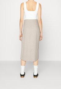 Krémová lněná midi sukně se střihem do rovna, bočními rozparky a hladkou texturou, kombinovaná s bílým topem na ramínka a černými botami.