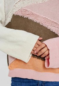 Pleteni pulover s horizontalnim blokovima boja u bijeloj, ružičastoj, smeđoj i narančastoj. Teksture i široki rukavi dodaju detalj.