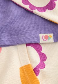 Bomullstyg i lavendel, krämfärg och orange med en texturerad våffelväv. Har blommönster i rosa och orange, med en etikettendetalj.