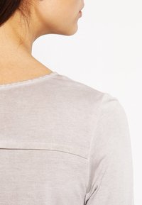 Maglietta a maniche lunghe grigio chiaro, realizzata in un tessuto morbido. Presenta un collo rotondo e un sottile dettaglio di cucitura sulla parte superiore della schiena.