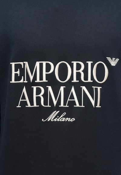 Czarna bawełniana koszula z dużym białym haftowanym napisem: "EMPORIO ARMANI" i "Milano" oraz emblematem logo w górnym prawym rogu.