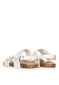 Sandalias de cuero blanco con una correa ajustable, plantilla de corcho y suela de goma, que presentan un diseño minimalista y una textura suave.