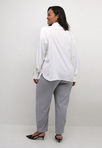 Hvid langærmet bluse med buet kant og strukturerede skuldre, parret med lysegrå tapered bukser og sorte slingback hæle.