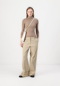Beige vide bukser med høj talje, parret med en tætsiddende brun turtleneck. Optræden suppleres med en hvid crossbody taske.