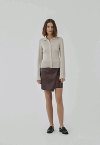 Beige ribbed knit cardigan with a collar and front buttons, paired with a dark brown leather wrap skirt and black loafers.