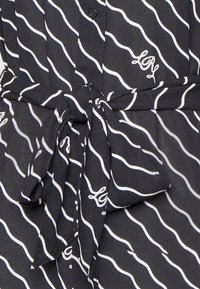 Black blouse with white wavy stripes, featuring a button front and tied waist detail. Includes small embroidered "Loy" logo.