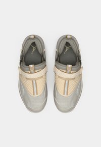 Αθλητικά παπούτσια σε μπεζ και ανοιχτό γκρι με υφασμάτινο επάνω μέρος με υφή, επενδεδυμένο κολάρο και κλείσιμο με λουράκι. Διαθέτουν πάνελ από πλέγμα και λογότυπο κοντά στη γλώσσα.