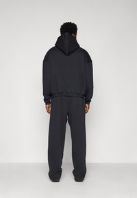 Fekete, oversized kapucnis pulóver nagy kapucnival, illesztve hozzá illő, laza fitted melegítőnadrággal. Puha, texturált anyagból készült, rugalmas mandzsettákkal.