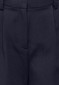 Gros plan sur un tissu bleu marine foncé avec une couture et une ceinture, probablement partie d'un pantalon tailleur ou d'un pantalon formel.