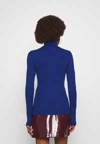 Niebieski sweter z golfem wykonany z delikatnego materiału, z długimi rękawami i dopasowanym krojem, w połączeniu z błyszcząca bordową spódnicą.