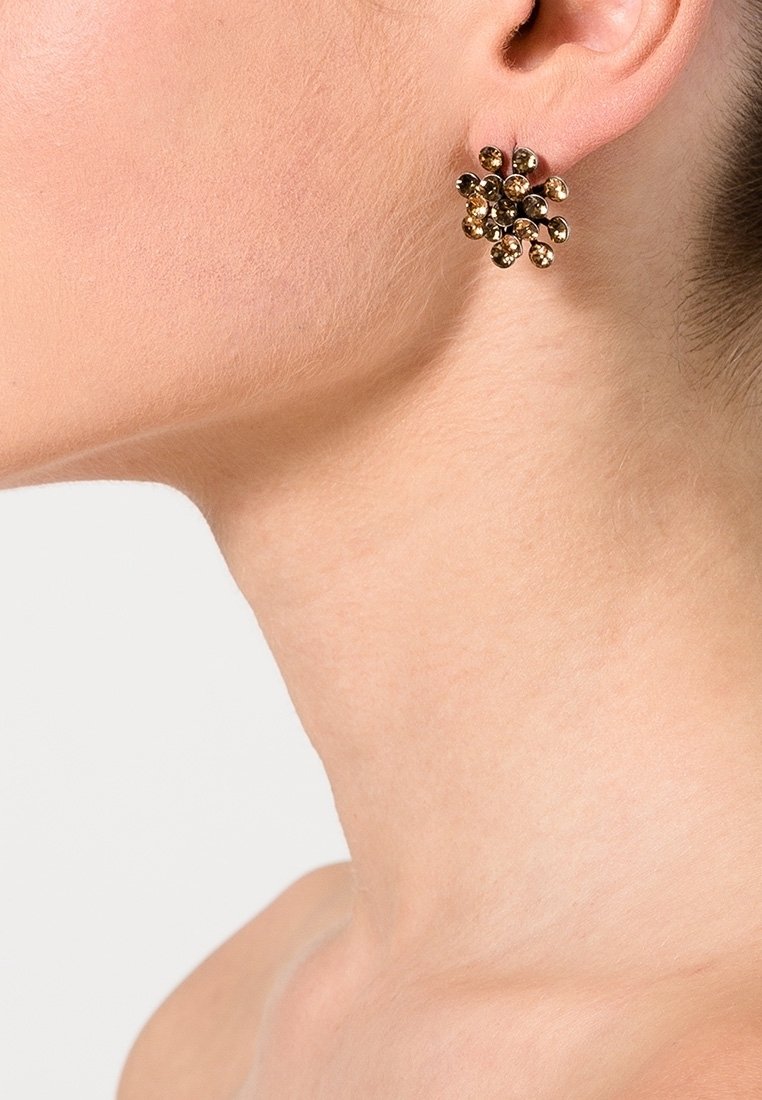 Cou et oreille d'une femme portant une boucle d'oreille clou en or avec plusieurs perles métalliques arrondies.
