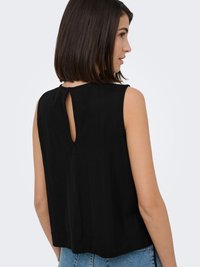 Woman with shoulder-length dark hair wears a sleeveless black top with a keyhole opening at the upper back and blue jeans.