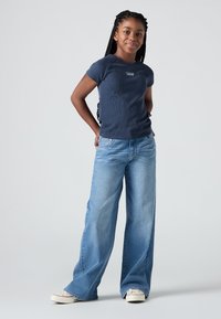 Ναυτικό μπλε ριγέ μπλούζα με κοντά μανίκια, σε συνδυασμό με ανοιχτό μπλε τζιν φαρδιάς γραμμής και λευκά αθλητικά παπούτσια. Απλό σχέδιο με λεπτομέρεια του λογότυπου της μάρκας.