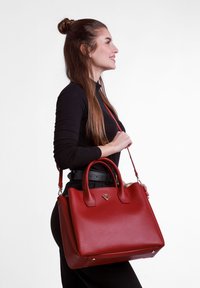 Rote Lederhandtasche mit strukturiertem Design, doppelten Griffen, abnehmbarem Schulterriemen und goldenen Hardware-Akzenten. Flacher Boden für Stabilität.
