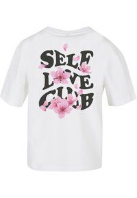 Bílá košile s krátkým rukávem se silným černým nápisem "SELF LOVE CLUB" a růžovými květy sakura rozptýlenými kolem nápisu.