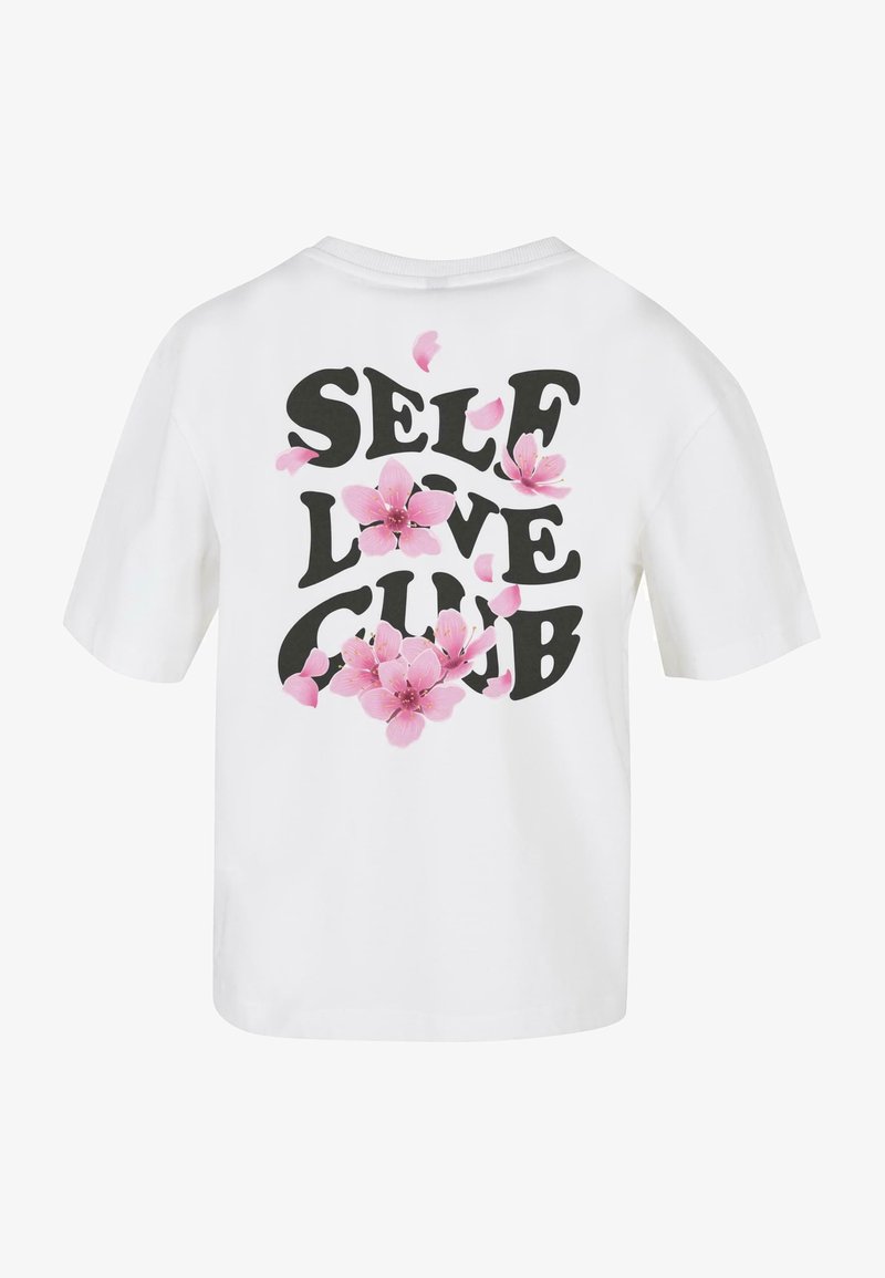 Bílá košile s krátkým rukávem se silným černým nápisem "SELF LOVE CLUB" a růžovými květy sakura rozptýlenými kolem nápisu.