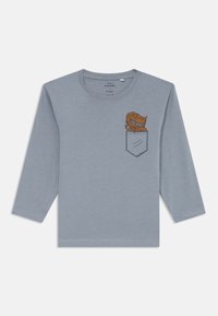 Hellblaues Langarm-T-Shirt aus weicher Baumwolle mit einer gesteppten Tasche, die ein oranges Dinosaurier-Motiv zeigt. Schlichter Rundhalsausschnitt.