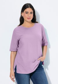 Lila T-Shirt mit kurzen Ärmeln, Rundhalsausschnitt, Seitenschlitzen und lockerer Passform, kombiniert mit dunkelblauen Jeans. Glatte Stofftextur.