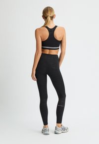 Reggiseno sportivo nero con motivo geometrico e design a schiena scoperta abbinato a leggings neri a vita alta con linee sottili e dettagli del logo bianco.
