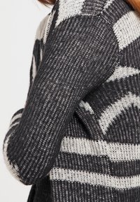 Pletený kardigan s černobílým pruhovaným vzorem, s texturovaným otevřeným tkaním a dlouhými rukávy.