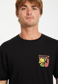 Sort bomulds T-shirt med et farverigt kranium og blomstermotiv på venstre bryst. Klassisk rund hals og korte ærmer.