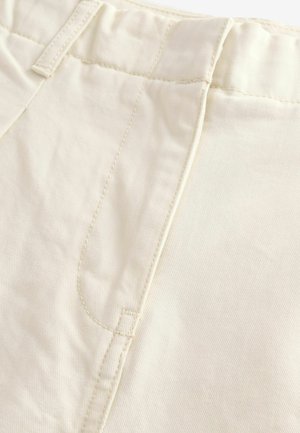Ces pantalons en coton beige clair présentent une texture lisse, des coutures discrètes aux poches avant et un design de taille classique sans embellissements supplémentaires.