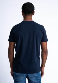 Námorně modré bavlněné tričko s kr�átkým rukávem, kulatým výstřihem a hladkou strukturou, zobrazené zezadu. Kombinováno se světle modrými džíny.
