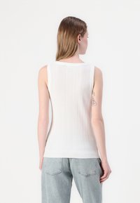 Hvit ribbestrikket singlett med rund hals og en tettsittende silhuett, kombinert med lyseblå baggy jeans. Minimalistisk design og myk tekstur.