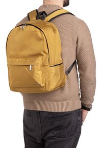 Sac à dos en nylon jaune avec des fermetures à glissi�ère, poche avant et accents noirs. Il dispose de bretelles rembourrées et d'une finition texturée.
