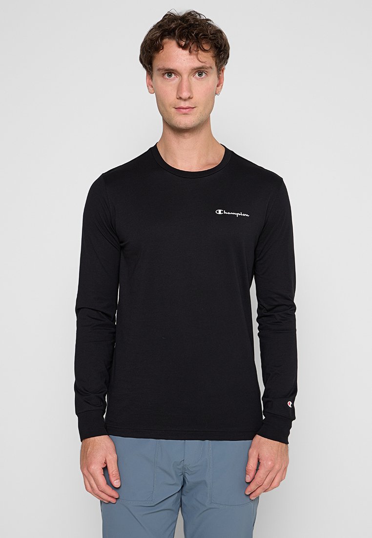 Camiseta negra de manga larga hecha de un tejido suave, con un escote redondo y un pequeño logo blanco de Champion en el lado izquierdo del pecho.