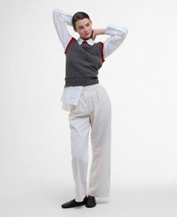 Gilet en maille grise avec des bords rouges sur une chemise blanche à col et un pantalon blanc ample, associé à des chaussures noires à enfiler.