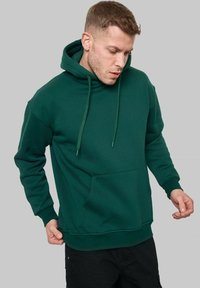 Hoodie en coton vert avec une poche avant, capuche à cordon de serrage et poignets côtelés. Texture douce et coupe décontractée.