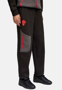 Schwarze Jogginghosen mit grauen Einsätzen, roten Reißverschlussakzenten und einem roten Logo. Hergestellt aus einem glatten Stoff, mit einer lockeren Passform und schmal zulaufenden Beinen.