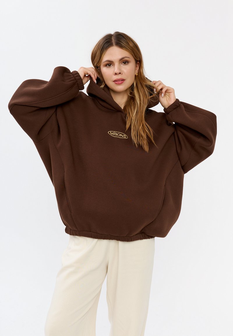 Bruine oversized hoodie met een trekkoordcapuchon, geribbelde manchetten en een cinched zoom. Bevat een klein gouden logo op de borst.
