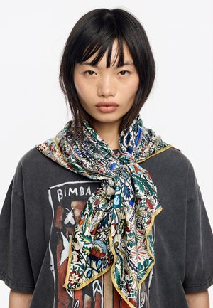 Foulard di seta con motivi floreali e fogliari colorati, legato attorno al collo, abbinato a una maglietta grigia con dettagli stampati.