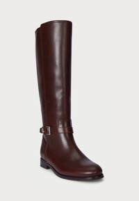 Bottine en cuir marron, haut comme le genou, au design épuré, agrémentée d'une sangle en boucle argentée et d'un petit talon bloc. Texture lisse avec des détails cousus.