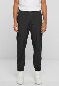 Pantaloni negri cu talie elastică, cu o croială lejeră, manșete îngustate și o textură ușoară, asortați cu adidași albi.
