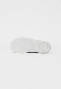 Bílá gumová podrážka boty s texturovaným gripem, obsahující embosovaný text "ENERGIA HUMANA" a kruhové logo; zakřivený tvar, hladké hrany.