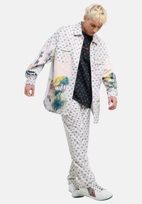 Witte casual outfit met een gestreepte overhemd met kleurrijke boomontwerpen, zwarte binnenlaag en bijpassende gestreepte broek.