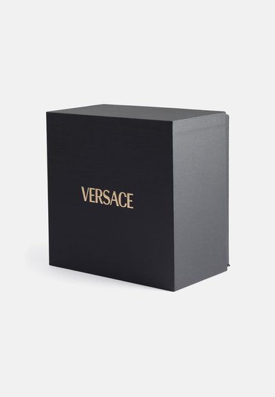 Scatola rettangolare nera con superficie testurizzata e logo dorato "VERSACE" sulla parte anteriore. Design chiuso, estetica minimalista.