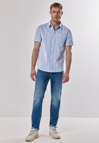 Korte mouw knoopshirt in lichtblauw met verticale witte strepen, gecombineerd met vervaagde blauwe jeans en witte sneakers.