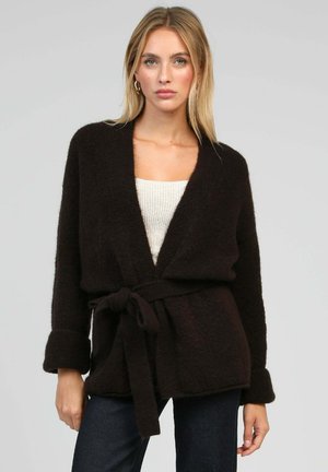Cardigan brun, duveteux, avec des manches longues, ceinture à nouer à la taille et devant ouvert. Tissu texturé et poignets profonds. Haut léger en dessous.