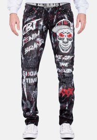 Jeans in denim nero con finitura strappata, caratterizzati da grafiche in stile graffiti bianche e rosse e un design di teschio. Accentuati con borchie.