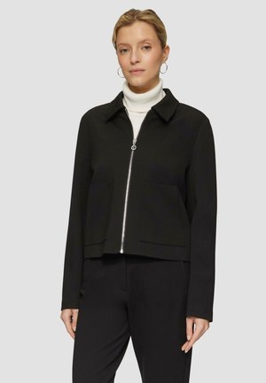 Zwarte cropped jack met een kraag, zilveren rits en twee voorzakken, gemaakt van glad, lichtgewicht stof. Gepaarde met een witte coltrui.