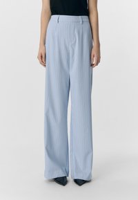 Pantaloni a gamba larga azzurro chiaro con righe verticali bianche, caratterizzati da una parte frontale piatta e una vestibilità sagomata in vita. Realizzati in un tessuto morbido.