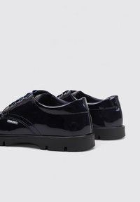 Zapatos de charol azul marino con perfil bajo, puntera redondeada y suela de goma negra texturizada. Incluye cordones negros y una marca sutil.