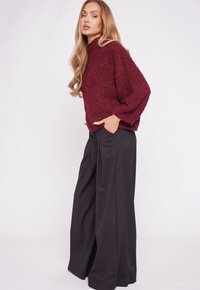 Burgundy, loose-knit sweater with a high neckline and wide sleeves, paired with black wide-leg trousers, featuring a smooth fabric.