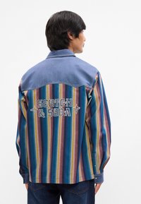 Τριχρωμο πουκάμισο με ρίγες από πολυχρωμο ύφασμα, που διαθέτει τζιν λεπτομέρειες και κεντημένο κείμενο "SCOTCH & SODA" στην πλάτη. Με κουμπωτές μανσέτες και άνετη εφαρμογή.